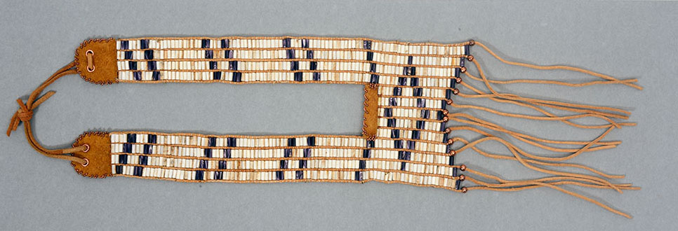 "Unity" Breastplate made of threaded white and purple quahog and whelk shell wampum beads. By Lydia Wallace Chavez Unity: A breastplate made of threaded white and purple quahog and whelk shell wampum beads. Leather backing and fastening ties. Synthetic thread used to weave beads onto leather strings. Leather strings/fringe decorate the bottom of the piece.